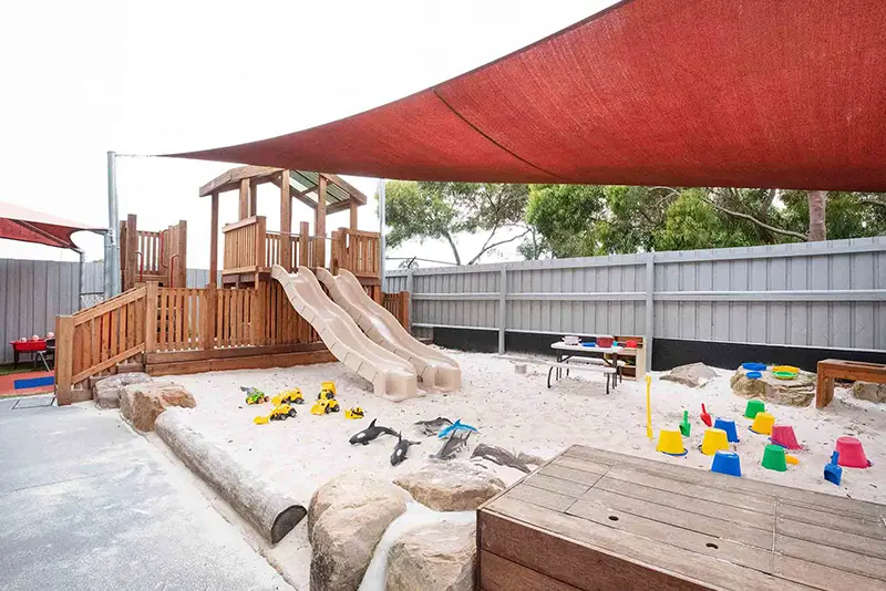 Shaded outdoor playground with slide and sandpit located at Busy Bees at Bentleigh East