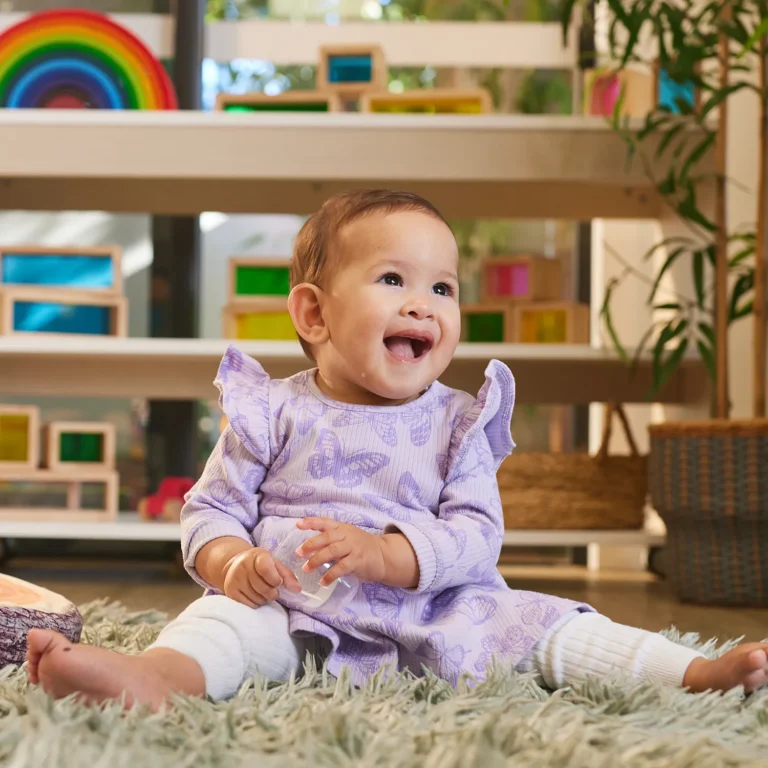 Baby sitting on fluffy rug at childcare.