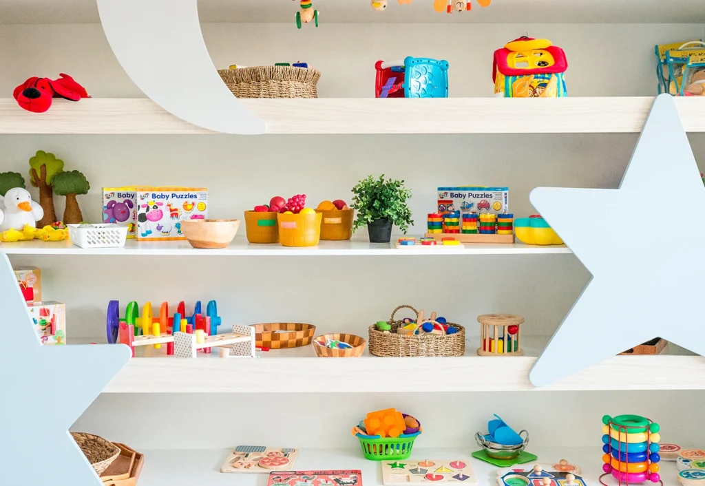 Shelves filled with colorful children's toys, including puzzles, blocks, stuffed animals, and toy fruits, all organized neatly against a backdrop with star and moon decorations.